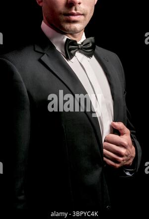 Ein Mann in schwarzem Anzug und Fliege passt seine Jacke an. Stockfoto