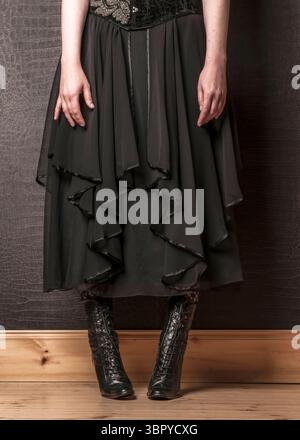 Eine Person trägt ein schwarzes Kleid und Stiefel. Stockfoto