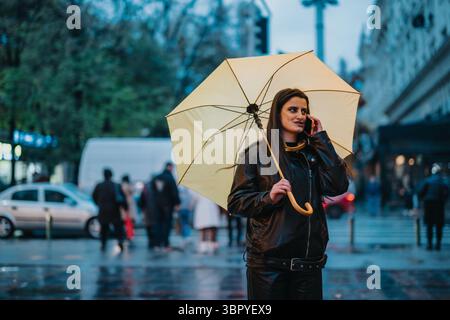 Frau, die mit einem gelben Regenschirm an einem regnerischen Stadtabend läuft Stockfoto
