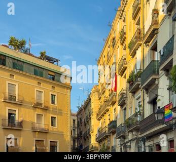 Die gelben Fassaden historischer Wohnhäuser in einem alten Viertel von Barcelona, Spanien, mit einer Regenbogenfahne, die von einem Balkon hängt. Stockfoto