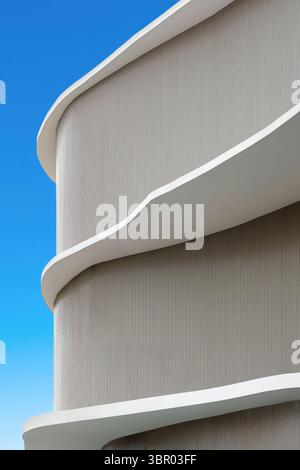 Abstraktes Detail eines modernen Gebäudes mit geschwungenen weißen Balkonen und einer strukturierten Fassade. Minimalistisches und futuristisches Architekturdesign gegen ein klares Stockfoto
