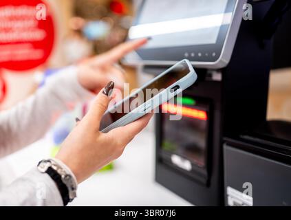 Frauenhände mit Smartphone bei Selbstkasse und Bezahlung von Einkäufen aus nächster Nähe Stockfoto