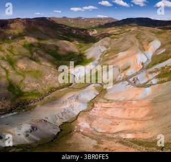 Blick aus der Vogelperspektive auf eine zerklüftete Landschaft, in der Erdtöne auf lebendige Grüns entlang eines sich windenden Flusses treffen, Grensdalur, Hveragerðisbær, Island. Stockfoto