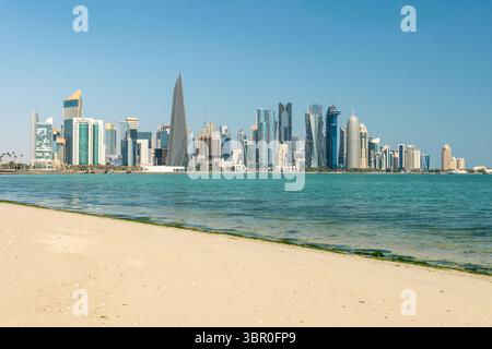 Weißer Sandstrand am Meer vor dem Hintergrund von Wolkenkratzern in Doha. Panoramablick auf die Skyline von Doha, Katar, an einem sonnigen Tag Stockfoto