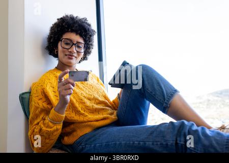 Afroamerikanerin mit Tablet und Kreditkarte beim Online-Shopping auf Bank um Fenster. Freizeitkleidung, Lifestyle, modern, Technologie, Entspannung, Stockfoto