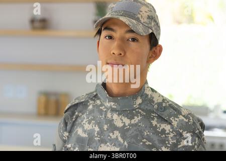 Asiatischer männlicher Soldat, der in der Küche neben Regalen steht, mit Gläsern, die eine digitale Tarnkappe tragen. Militär, Uniform, zeitgenössisch, Innenraum, tactica Stockfoto