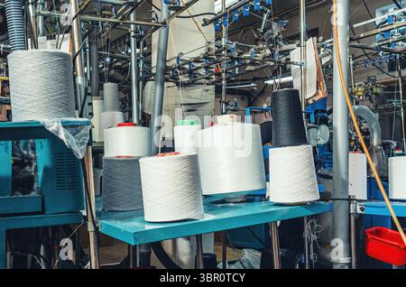Weiße graue und schwarze Gewinde auf den Spulen bei Maschinen. Industrieunternehmen zur Herstellung von Socken. Moderne Technologien Stockfoto