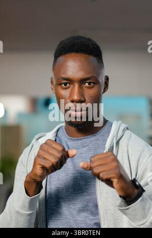 Afroamerikaner posiert in Boxstellung im Fitnessstudio mit Reißverschluss Hoodie, T-Shirt, Smartwatch. Athlet, Fitness, Kraft, Entschlossenheit, Motivation, Stockfoto