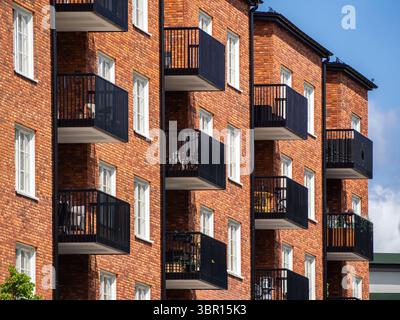 Blick aus der Nähe auf moderne Apartmentgebäude mit roten Backsteinfassaden und schwarzen Balkonen. Die Architektur zeigt ein zeitgenössisches Design mit m Stockfoto