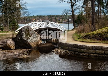 Weiße Bogenbrücke über einen kleinen Kanal und einen sandigen Pfad, der in einem Stadtpark dorthin führt. Stockfoto