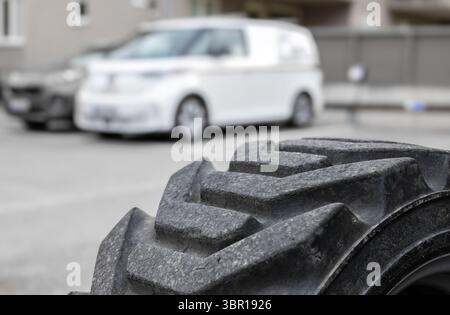 Nahaufnahme eines robusten Reifenprofils mit einem verschwommenen weißen Lieferwagen im Hintergrund, der den städtischen Nahverkehr zeigt. Stockfoto