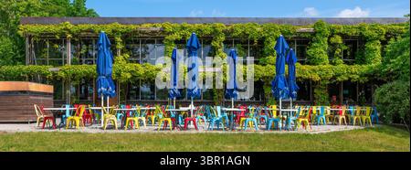 Stockholm, Schweden - 10. Juni 2025: Eine lebhafte Café-Szene im Freien mit bunten Stühlen und Tischen unter großen blauen Sonnenschirmen. Das Café ist umgeben Stockfoto