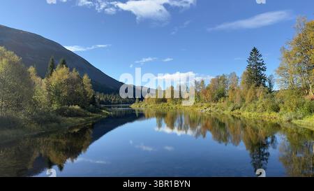 Der ruhige Fluss reflektiert die schönen Herbstfarben unter einem klaren blauen Himmel. Stockfoto