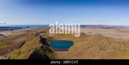Aus der Vogelperspektive auf einen ruhigen, türkisfarbenen See, eingebettet in zerklüftete, braune Hügel unter klarem Himmel, trifft auf das ferne Meer, Grindavik, Grindavíkurbær, Island. Stockfoto
