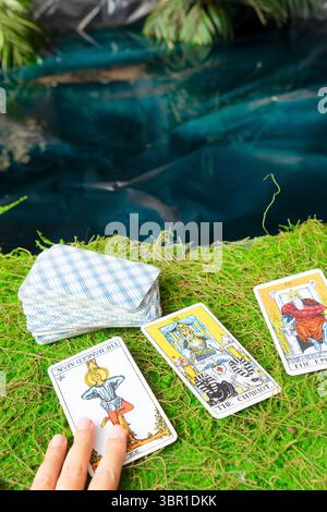 Ein wunderschönes Arrangement von Tarot-Karten verteilt auf weichem Gras neben einem friedlichen und ruhigen Wasserkörper Stockfoto