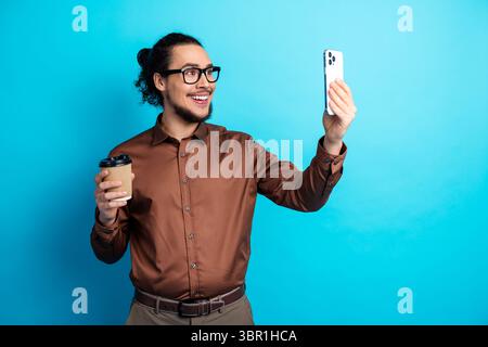 Junger Geschäftsmann mit Kaffee, der moderne Kommunikation auf dem Smartphone vermittelt, trendig und stilvoll in formeller Kleidung Stockfoto