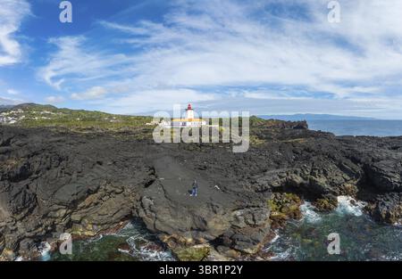 Aus der Vogelperspektive des berühmten Leuchtturms, der über der zerklüfteten, dunklen vulkanischen Küste wacht, während die Wellen darunter stürzen, Vulkankrater Pico, Azoren, Portugal. Stockfoto