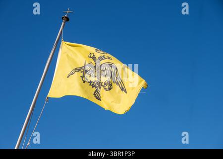 Das byzantinische Reich und die griechisch-orthodoxe Kirchenflagge winken auf blauem Himmel. Doppelköpfiger Adler auf gelb Stockfoto
