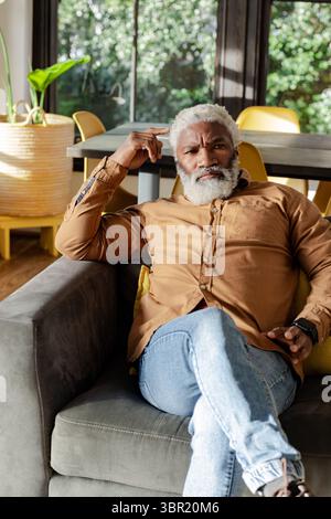 Ranghoher afroamerikanischer Mann, der sich auf dem Sofa im Wohnzimmer zurücklehnt und die Smartwatch an gelben Stühlen überprüft. Luxus, Entspannung, modern, Innenraum, Komfort, lei Stockfoto