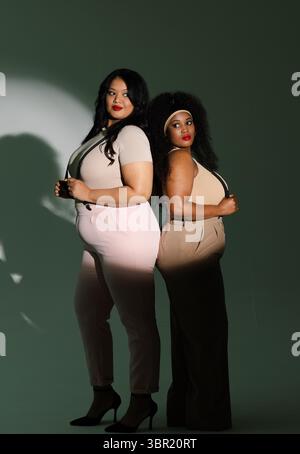 Verschiedene Freundinnen stehen im Studio zurück an Rücken und tragen schwarze Hosenträger mit Haarband High Heels. Mode, Selbstvertrauen, Stil, Professionalität, Leg Stockfoto