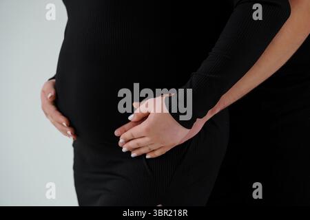 Nahaufnahme der Hände einer schwangeren Frau, die ihren abgerundeten Bauch in einem engen, schwarzen Rippenoutfit hüllen und einen zarten Moment der Erwartung darstellen Stockfoto