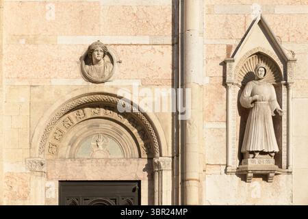 Seitenportal mit Lünette und Statue von Alberto V d'Este in Nische an der Marmorfassade der Kathedrale von Ferrara, Ferrara, Italien. Stockfoto