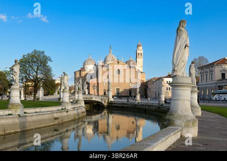 Blick auf den Prato della Valle in Padua, Italien, mit Statuen am Kanal und der Basilika Santa Giustina im Hintergrund. Stockfoto