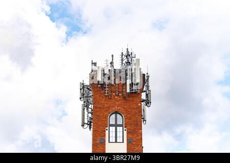 Moderne Antennen für Mobilfunknetze und Geräte, die an einem alten Backsteinturm befestigt sind. Ein Kontrast zwischen historischer Architektur und moderner Technologie. Stockfoto