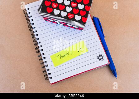 Vielen Dank, dass Dankeschön mit blauem Stift und einer Geschenkbox mit roten und weißen Herzen auf Notizbuchhintergrund steht Stockfoto