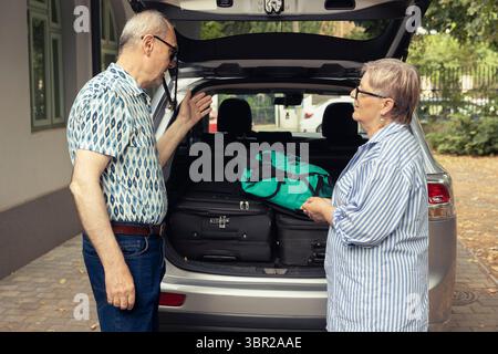 Glückliches älteres Paar bereitet sich auf einen Roadtrip vor und organisiert Reisetaschen im Kofferraum. Fröhlicher Lebensstil im Ruhestand mit Entdeckungsreise in die Natur und Outdoor-Spaß mit Lebenspartner. Stockfoto