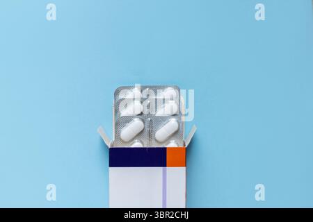Offene Medizin-Box mit weißen Pillen in Blisterpackungen auf blauem Hintergrund. Gesundheitswesen, Behandlung Und Pharmazeutisches Konzept. Flat Lay-Bild Mit Kopieren Stockfoto