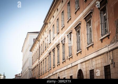 Schräge Perspektive auf die verwitterte Wohnfassade aus dem 19. Jahrhundert in der Altstadt von Triest, Italien, mit abblätterndem ockerfarbenen Putz, hohen Fensterläden und Stockfoto
