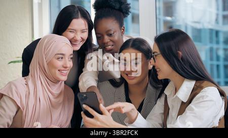 Glückliches Lachen multiethnische Frauen Frauen arbeiten Team Mädchen afroamerikanisch japanisch arabisch muslimisch Hijab Geschäftsfrauen, die Handy-Gebrauch suchen Stockfoto