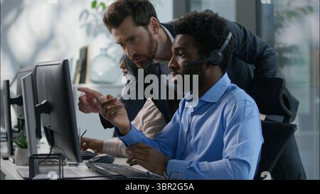 Vielfältige Callcenter-Zusammenarbeit kaukasischer Chef erklärt Aufgabe Zeigefinger afrikanisches Headset für Mitarbeiter indischer weiblicher Arbeitscomputer Geschäftsanruf Stockfoto