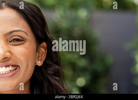 Indische Frau lächelt im Garten und zeigt silberne Ohrstecker und Hemdkragen aus Denim, Kopierraum Stockfoto