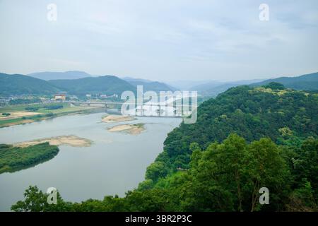 Gongju, Südkorea - 13. Juni 2025: Von der Bergfestung Gong aus betrachtet fließt der Geum River an bewaldeten Hügeln und Sandbänken vorbei, mit einem Paar bridg Stockfoto