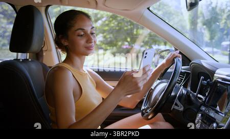 Afroamerikanerin weibliches Mädchen, das Handy Smartphone Auto Auto Autofahrer Online-Chat soziale Medien Netzwerke lächelnde Technologie hält Stockfoto