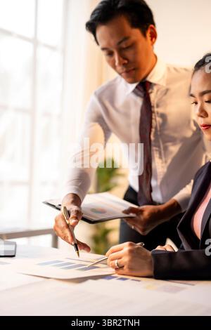 Ein Mann und eine Frau sitzen mit Papieren und einem Stift an einem Tisch. Die Szene ist fokussiert und ernst, da die beiden Personen gemeinsam an einem Projekt arbeiten Stockfoto