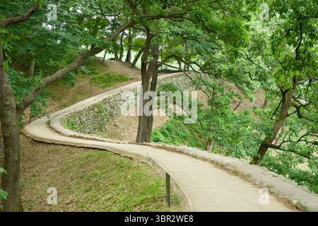 Gongju, Südkorea - 13. Juni 2025: Ein schmaler, gewundener Pfad folgt der Steinmauer der Gongsanseong-Festung und führt sanft durch einen schattigen Hügel Stockfoto
