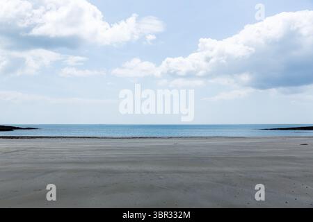 Die breite, nasse Sandküste erstreckt sich in flachem Design, mit ruhigem Meer, bewölktem Himmel und felsigen Felsvorsprüngen Stockfoto