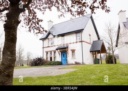 Freistehendes zweistöckiges Haus in flachem Design mit blauer Tür, geschwungener Auffahrt und grünem Rasen Stockfoto