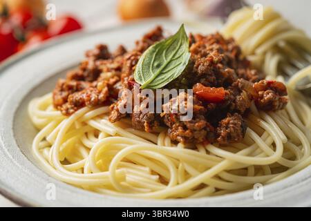 Pasta Spaghetti Bolognese mit Rinderhacksauce, Tomaten, Parmesankäse und frischem Basilikum auf einem Teller auf weißem Fliesenhintergrund. Italienisches Essen Stockfoto