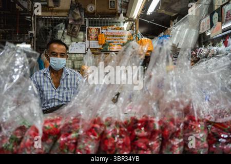 Bangkok, Thailand. Juli 2025. Ein Mann mit einer Gesichtsmaske steht in seinem Laden, mit Blumengirlanden in Plastiktüten, die im Vordergrund sichtbar sind. Jeden Morgen laufen buddhistische Mönche in Bangkok durch die Straßen, um Almosen, Essen und Blumen von den Laien zu erhalten. In der Nähe, auf dem Yodpiman Blumenmarkt, werden Blumen für diese täglichen Rituale zubereitet und verkauft, die in der buddhistischen Tradition Theravada verwurzelt sind. (Foto von Ploy Phutpheng/SOPA Images/SIPA USA) Credit: SIPA USA/Alamy Live News Stockfoto