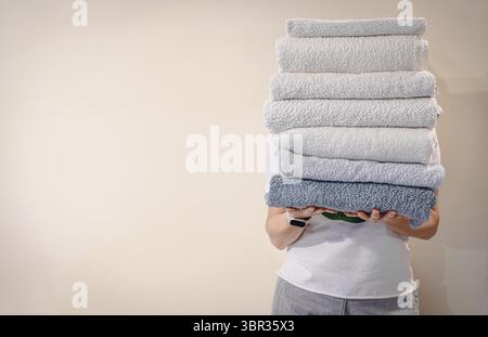 Frau hält einen Stapel sauberer weißer Badetücher auf Heller Hintergrund Stockfoto