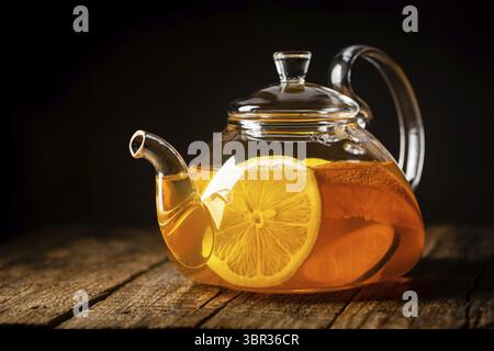 Glas Teekanne mit heißem Zitrustee aus Orangen, Zitronen und Limetten, gesundes Getränk auf dunklem Hintergrund Stockfoto