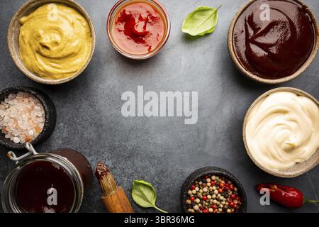 Klassische Saucen, amerikanischer gelber Senf, Ketchup, Barbecue-Sauce, Mayonnaise auf schwarzem Steinhintergrund, Draufsicht mit Kopierraum Stockfoto
