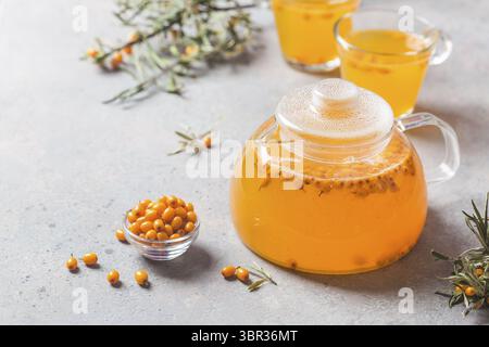 Vitaminic gesunden Sanddorn Tee in einer Teekanne aus Glas mit frischen, rohen Sanddornbeeren auf grauem Stein Hintergrund Stockfoto
