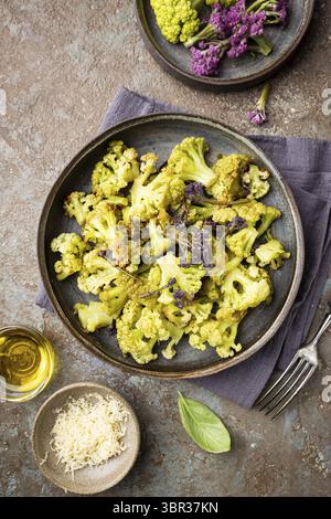 Gebratener grüner und lila Blumenkohl mit Kräutern und Gewürzen auf Teller über grauem Steinhintergrund. Draufsicht Stockfoto
