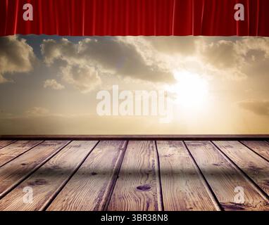 Die flache Designbühne zeigt Holzdielen und einen roten Samtvorhang unter sonnendurchfluteten Wolken Stockfoto