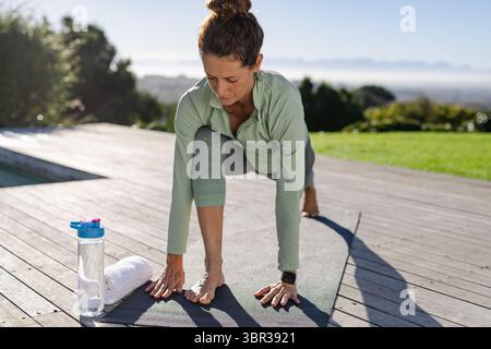 Frau, die auf dem Pooldeck mit Yogamatte, Wasserflasche, Fitnessuhr nach vorne geht Stockfoto